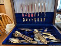 Silver tone Community brand flatware in dark blue velvet lining inside a case with slots for knives in the lid and spoons and forks in the base.