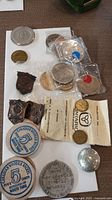 Overview photo showing an assortment of medallions, tokens, coins, pins and a button arranged on a table.