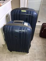 Two navy blue Heys hard case rolling suitcases pictured standing upright side by side on a tiled floor in a bathroom or laundry room setting.