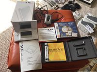 Wide view showing Nintendo DS Lite console, Brain Age game in case, instruction booklets, and charging cable.