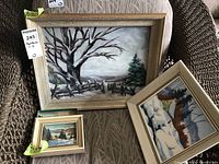 Large framed winter landscape painting with bare trees and fenced path on a chair
