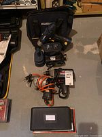 Wide view showing Mastercraft cordless drill with battery, battery charger, Craftsman corded drill coiled with orange cord, Black & Decker drill, black carrying bag, and small black case.