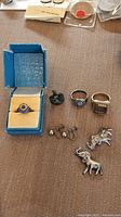 Photo showing two elephant pins, three rings including one in a blue box, pair of screw-on earrings, and damaged pendant.