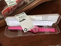 Hot pink Swatch watch with pink strap inside original transparent plastic case, visible auction tag.