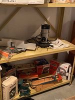 Black & Decker router with owner manual, small electric heater box, boxed jigsaw, and boxed electric sander along with hand tools on shelving