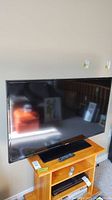 Front view of the 50" Samsung UN50J6200AF LED TV on a wooden stand with remote placed on stand shelf