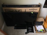 Insignia LED TV with remote control, user manual, and wall mount components displayed in front of the original box.