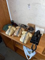 Six vintage phones on wooden shelf; four beige table top rotary phones, one black wall mount rotary phone, cords wrapped around each phone.