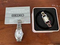 Seiko watch and instruction manual alongside Fossil watch in box on wooden surface