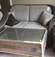 Wicker sofa with beige cushions and two throw pillows, one matching cushion and one dark brown.