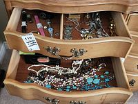 Open wooden jewelry box showing top two drawers with assortment of ladies wristwatches and costume jewelry including necklaces and bracelets.