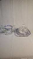 Photo showing clear glass sugar bowl with two handles and blue Greek key pattern and butter dish with hexagonal plate and dome lid.
