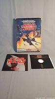 Original 1987 Star Wars game box with colorful space battle artwork, floppy disk, and information booklet arranged on flat surface.