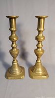 Full view of the pair of brass candlesticks standing side by side on a flat surface.