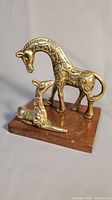 Pair of brass giraffe figures (one standing, one laying) on wooden base.