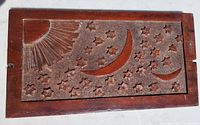 Top-down photo of rectangular mahogany panel carved with a radiant sun in upper left, crescent moons, and many stars on textured background.
