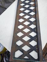 Cast iron lattice panel laid flat on a white surface showing diamond lattice design and signs of rust and wear.