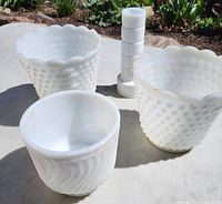 Four white milk glass items including two hobnail pattern planters, one swirl patterned planter, and a tall vase.