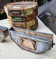 Stack of five rusty steel film canister cases with worn old labels on each side, taken outside on table showing surface wear and rust.