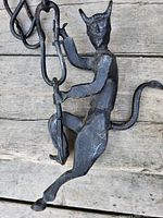 Photo of the iron devil sculpture climbing a chain, showing the front and side views of the figure and the link chain details on a wooden surface.