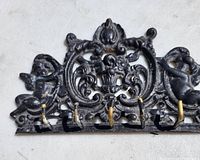 Top front view of ornate brass key hooks painted black, showing six hooks and detailed Victorian style decorations with cherub angels.