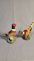 Pair of pheasant salt and pepper shakers together showing different poses on light background.