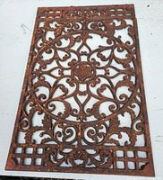 Full view of rectangular rusty ornamental floor grill with intricate scrolling pattern and center floral rosette