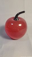 Full view of the red glass apple paperweight with black stem.
