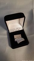 Sterling silver CIBC pin placed inside open black velvet presentation box showing front of pin and interior lining.