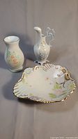 Photo showing all three pieces: a tall floral vase, ornate floral ewer, and shell-shaped dish with gold trim