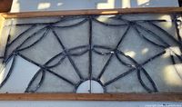 Full view of one leaded glass window showing the spider web fan pattern in black lead cames with wavy pressed glass and a wooden frame.
