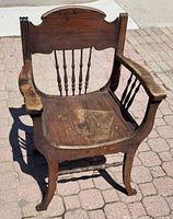 Front angle view of the Victorian wooden chair showing spindle backrest, armrests, seat, and leg shape on patio blocks.