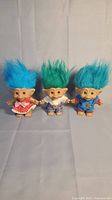 Photo of three vintage troll dolls with colorful hair and gemstone navels against a plain background.