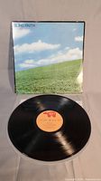 Photo of album cover and vinyl record showing cover art with a grassy hill and cloudy sky and the vinyl record placed in front.