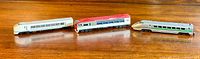 Three 1/130 scale Japanese model trains arranged side by side on a wood surface