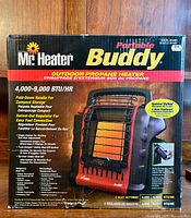 Front face of original packaging showing image of heater, brand Mr. Heater Portable Buddy, model MH9BX, heat output 4,000-9,000 BTU/hr, fold-down handle, swivel-out regulator, simple controls.