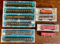 Photo of six passenger cars in original blue foam casing and seven stock cars in clear plastic cases on a wooden surface.
