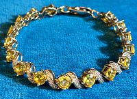 Photo showing the full length of the tennis bracelet laid flat to showcase the alternating yellow citrine CZ and clear CZ stones in a silver setting.