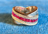 Close-up image of the sterling silver crossover ring showing red and clear cubic zirconia stones on a blue fabric background.