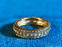 Close-up front 3/4 angle of gold wash sterling silver half eternity ring with cubic zirconia stones on blue fabric background.