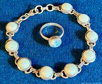 Photo showing the vintage Larimar tennis bracelet and matching ring against a dark blue fabric background. The bracelet features multiple round light blue Larimar stones set in sterling silver bezels linked together. The ring has a matching round Larimar stone set in sterling silver band.