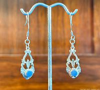 Full view of both earrings hanging on a display stand showing the intricate sterling silver design with a blue round stone.