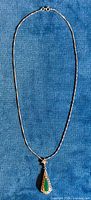 Full view of the necklace and pendant laid flat on a blue fabric background