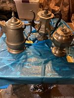 Overview of the three antique coffee pots on a blue plastic-covered table showing size and design differences