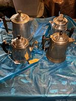 Four antique coffee pots displayed on a blue surface showing various sizes and shapes and handles.