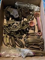 Boxed assortment of antique-style metal drawer pulls and handles seen from above, showing varied shapes, sizes and designs.