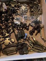 Photo showing a box with various antique brass and metal dresser pulls, including ornate designs and mounting screws.