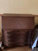 Front view of antique wooden dresser with rich dark finish, showing four curved drawers with ornate metal handles and closed top fold-down section with a keyhole.