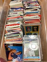 Plastic bin filled with rows of sports cards, mostly baseball cards, showing players like Tommy John and others in the front rows.