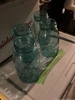 Four blue-tinted glass quart Mason jars arranged on a surface, showing the embossed 'Ball' logo and clear screw-top rims.